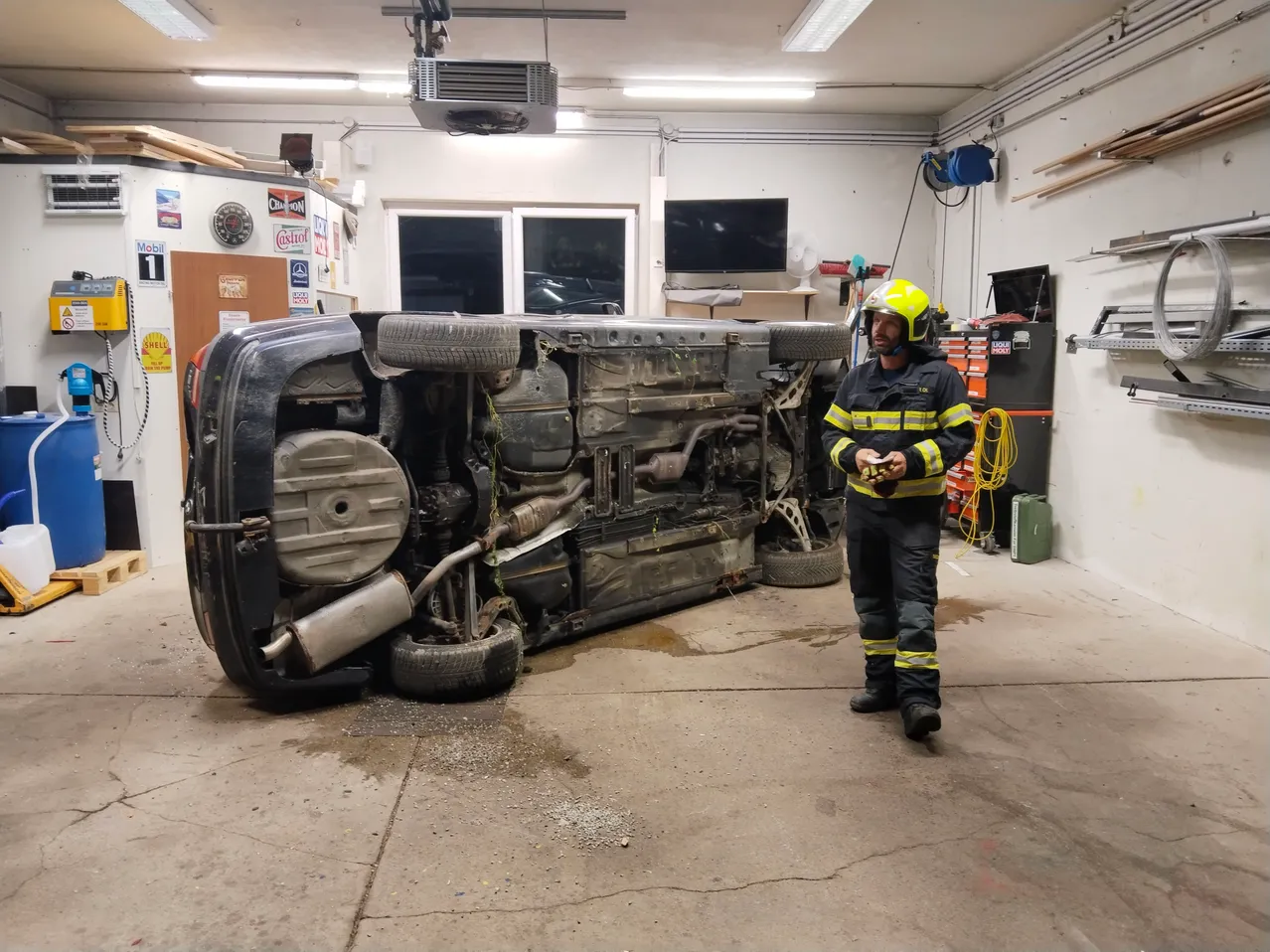 Ein Feuerwehrmann steht neben einem umgestürzten Auto in einer Garage.