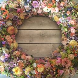 Ein farbenfroher Kranz aus verschiedenen Blumen und Blättern auf einem hölzernen Hintergrund.