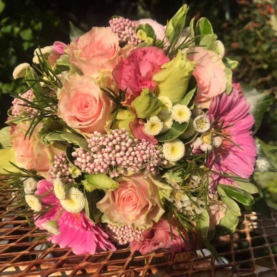 Ein lebiger Blumenstrauß aus rosa und weißen Blumen, einschließlich Rosen, Gänseblümchen und anderen Blüten, auf einer rustikalen Metalloberfläche arrangiert.