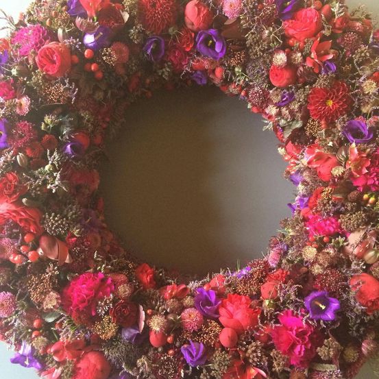 Ein Kranz aus getrockneten Blumen in Rot-, Lila- und Rosatönen mit einer kreisförmigen Öffnung in der Mitte.