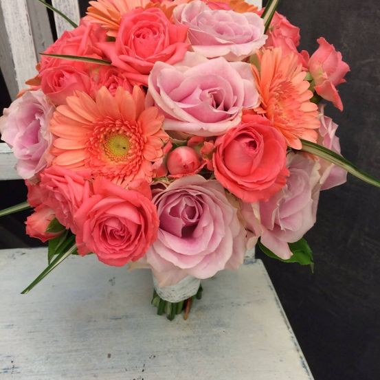 Ein leuchtender Strauß aus rosa und orangefarbenen Blumen, einschließlich Rosen und Gerbera, auf einer weißen Oberfläche angeordnet.