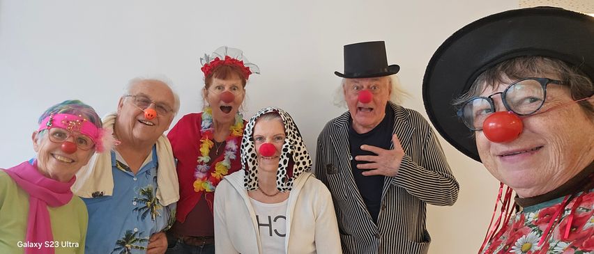Vier Erwachsene in Clown-Kostümen posieren für ein Foto. Die Frau in der Mitte trägt eine Kapuze mit Punkten und der Mann rechts einen schwarzen Zylinder. Die Frau links hat eine rote Clownnase und eine Blumenkopfbedeckung.