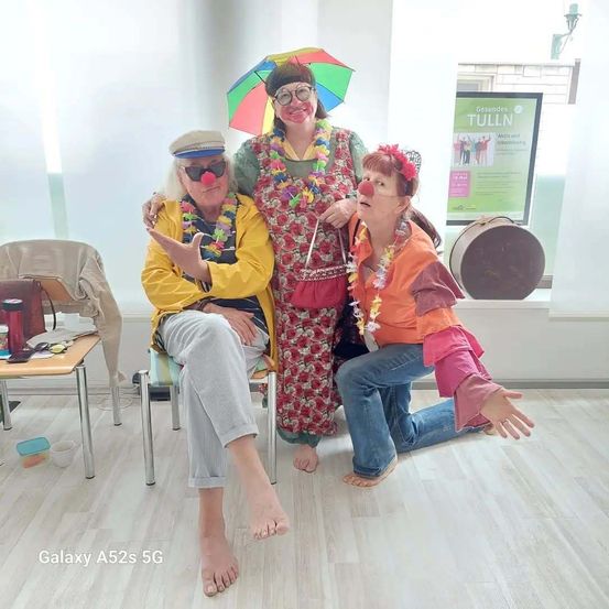 Drei Clowns posieren für ein Foto in einem Raum. Einer kniet, einer sitzt und der dritte steht mit einem Regenschirm.