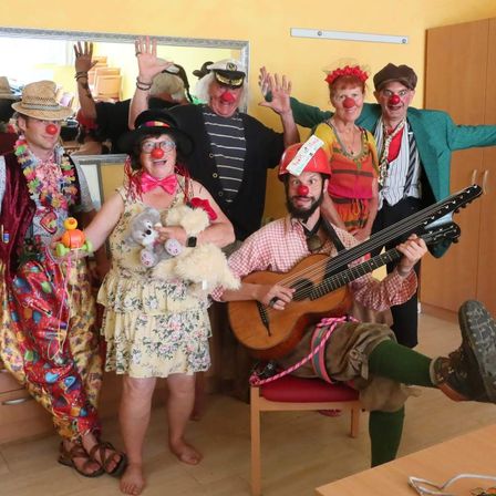 Eine Gruppe von Menschen, die als Clowns verkleidet sind, posiert für ein Foto. Ein Mann spielt Gitarre, während andere Spielzeuge halten.