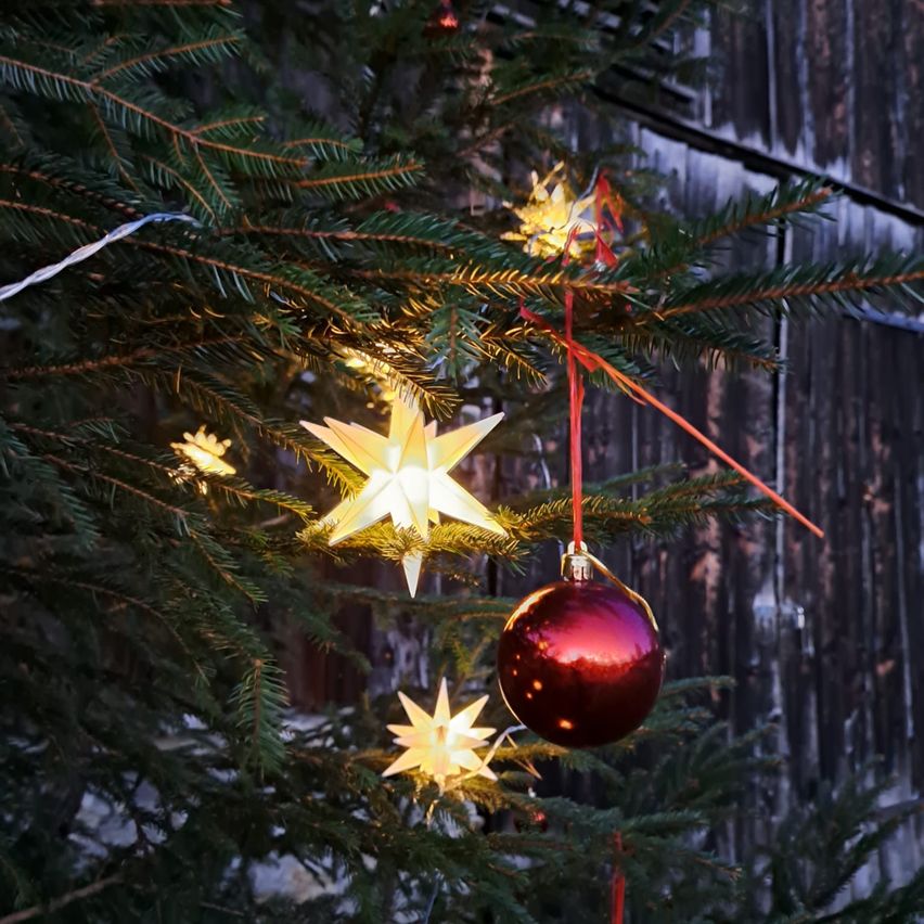 Ein Weihnachtsbaum mit Lichtern und Dekorationen, einschließlich einer roten Kugel, Sternen und einem hölzernen Hintergrund.