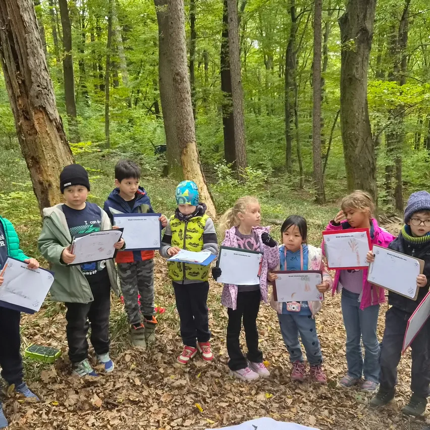 Eine Gruppe von Kindern im Wald, die Papiere halten und etwas vor sich betrachten.