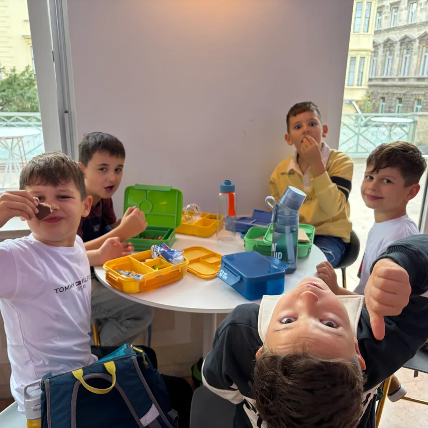 Fünf Jungen sitzen um einen Tisch herum, essen und lächeln. Ein Junge gibt einen Daumen hoch.