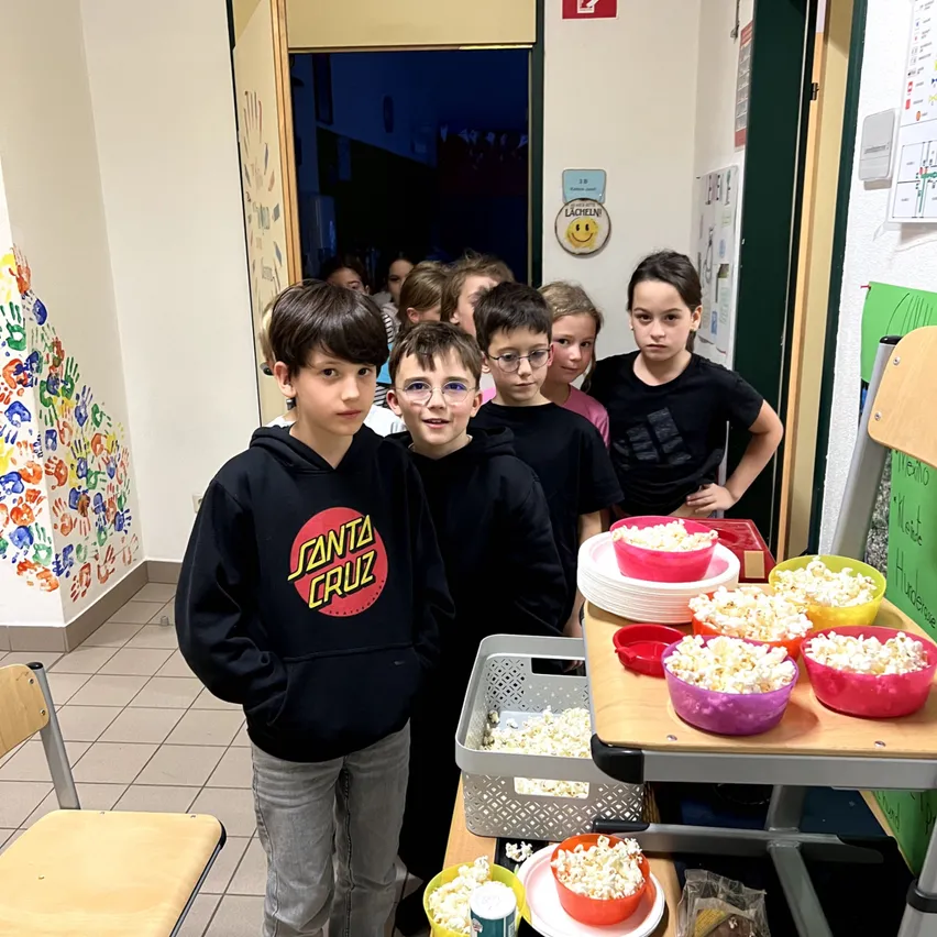 Schulkinder stehen Schlange für Popcorn in bunten Schalen in einem Schulflur.