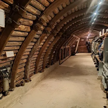 Ein langer Tunnel mit Holzbalken und Betonboden. Am Ende steht eine Person.