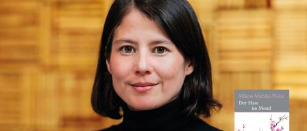 A smiling woman with short black hair, wearing a black turtleneck. A book titled 'Der Hase im Mond' is visible in the background.