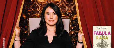 A woman stands with hands raised near a red curtain, wearing a black dress. Behind her, a gold-themed wall and chandelier. A book titled 'FA' is partially visible on the right.