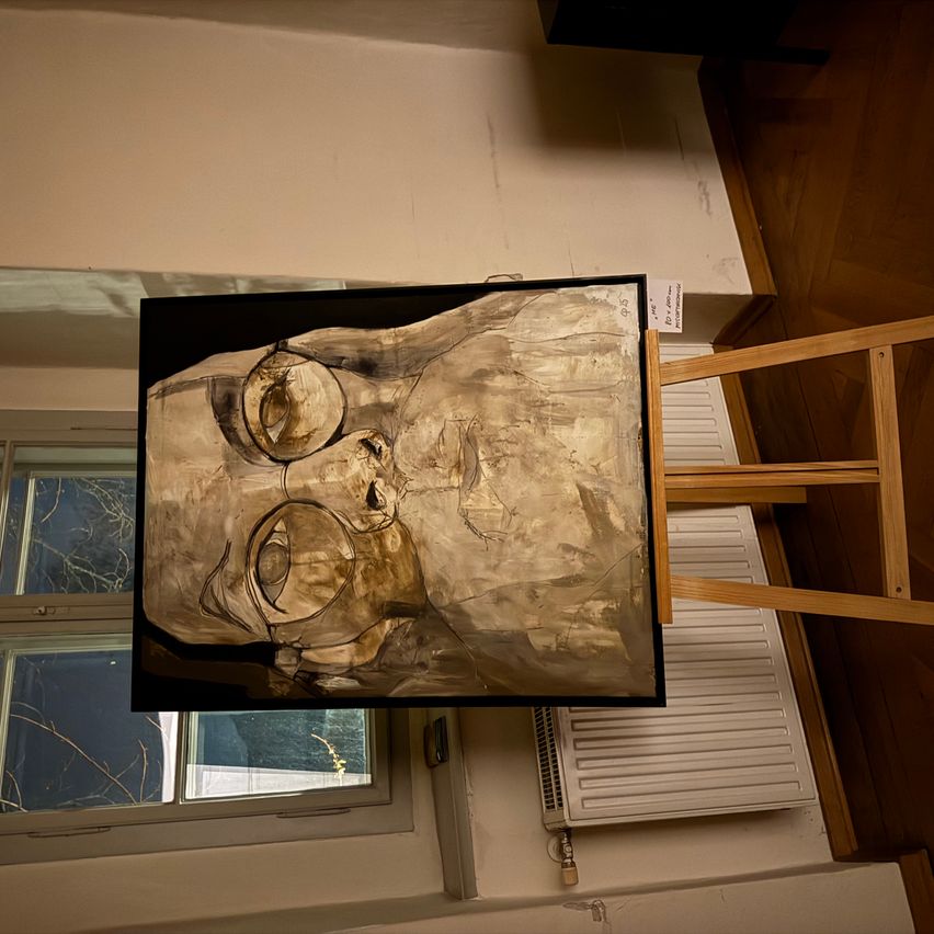 Ein großes abstraktes Gemälde, das ein menschliches Gesicht darstellt, hängt in einem Raum mit Holzboden und Fenster. Das Gemälde wird von einem Holzständer gestützt.