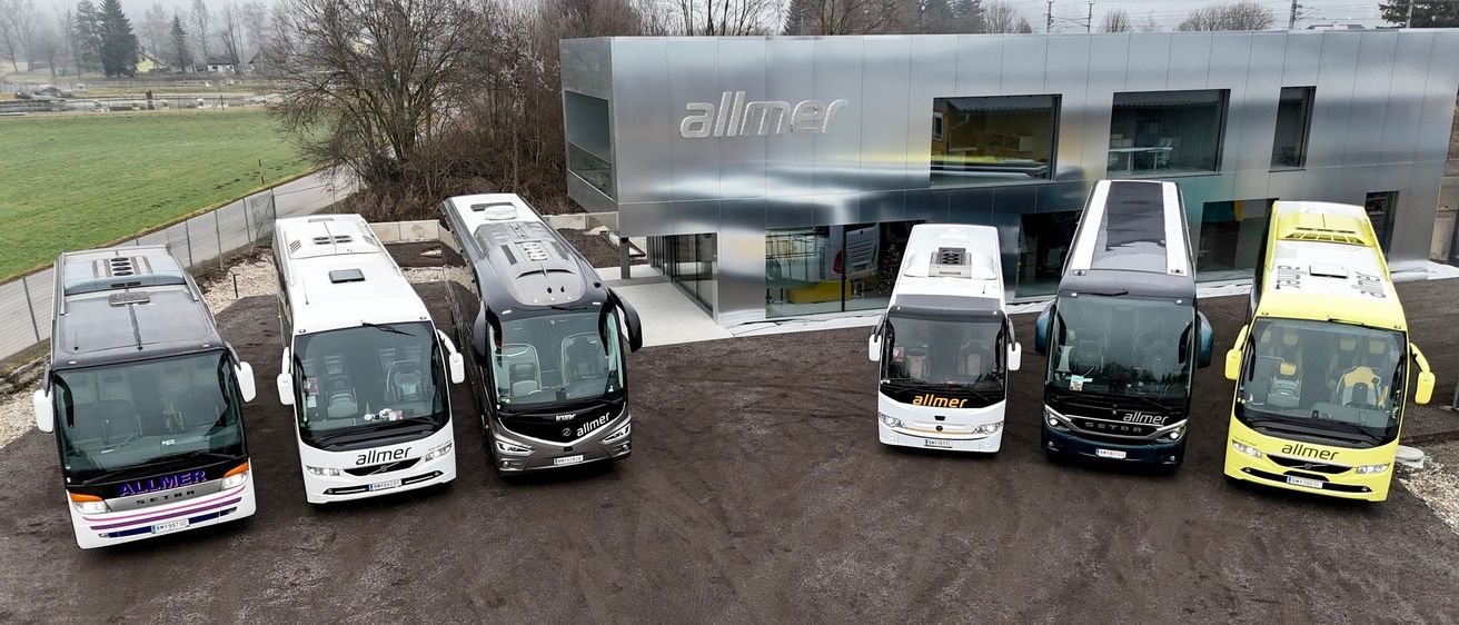 Vier Allmer-Busse sind vor einem Gebäude geparkt, auf dem der Schriftzug Allmer steht. Die Busse sind auf einer Betonfläche geparkt.