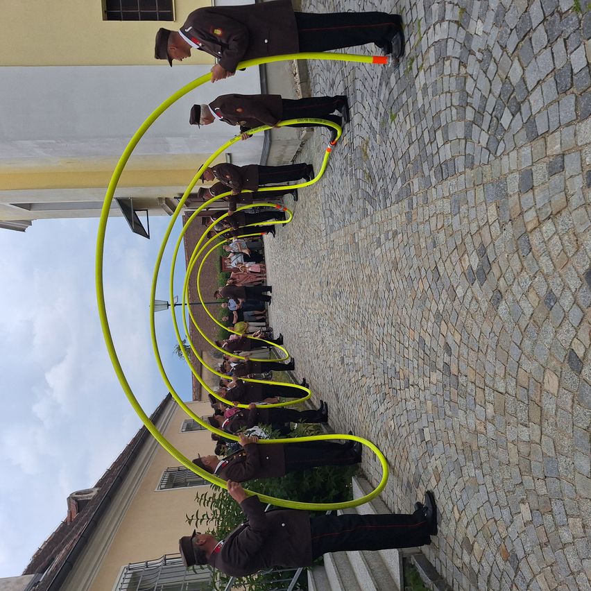 Eine Gruppe von Menschen in Uniform führt eine Formation mit gelben Hula-Hoops auf einer Kopfsteinpflasterstraße durch.
