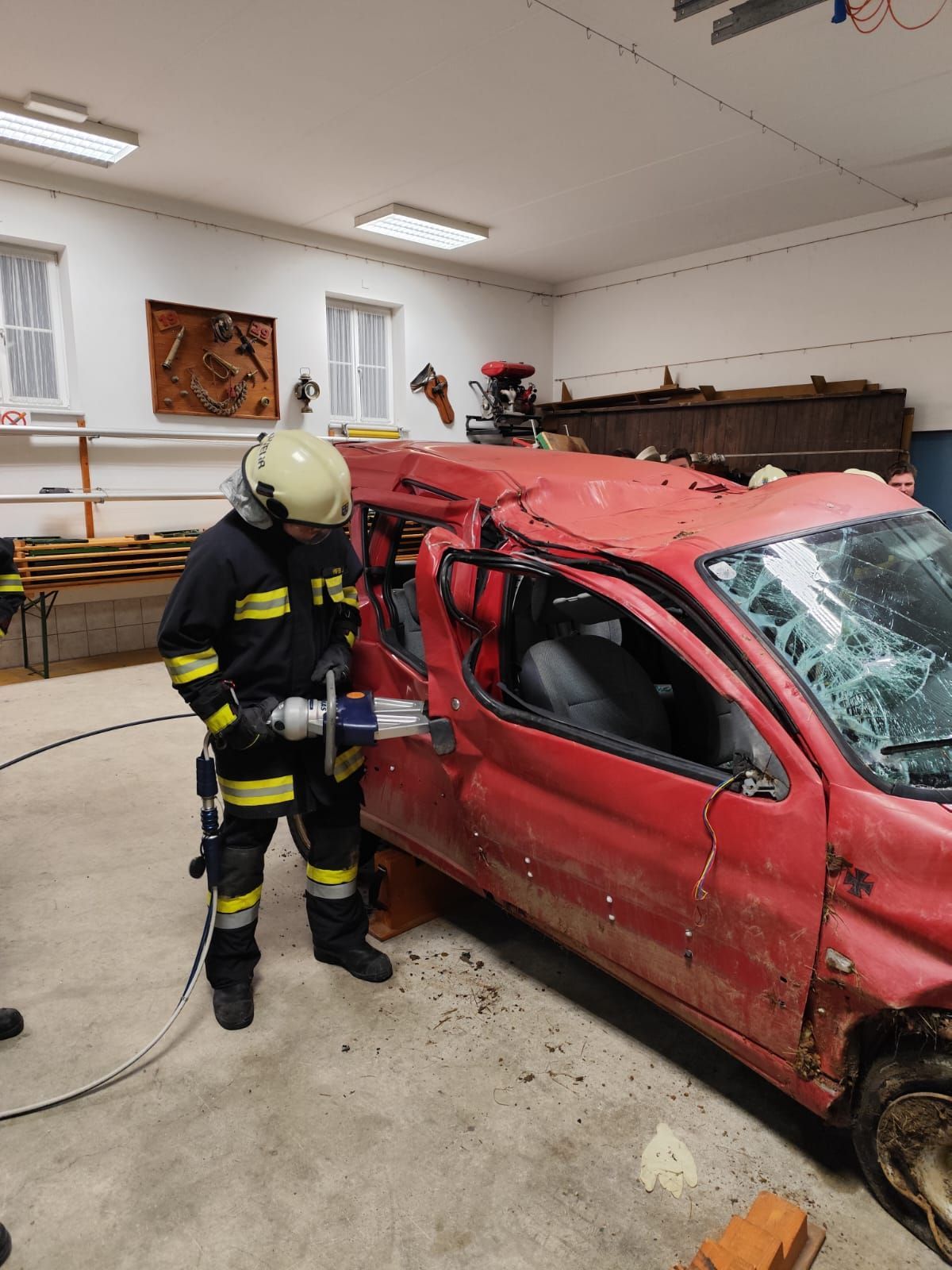 Ein Feuerwehrmann benutzt ein hydraulisches Schneidewerkzeug an einem beschädigten roten Auto mit zerbrochener Windschutzscheibe in einer Garage.