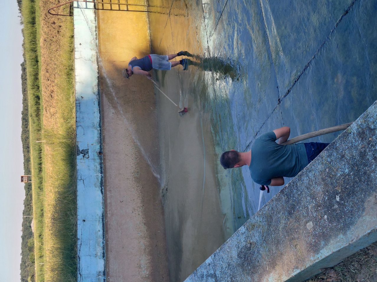 Zwei Männer reinigen ein großes Wasserreservoir, einer auf der linken Seite mit einem Schlauch und einer auf der rechten Seite mit einem Schlauch.