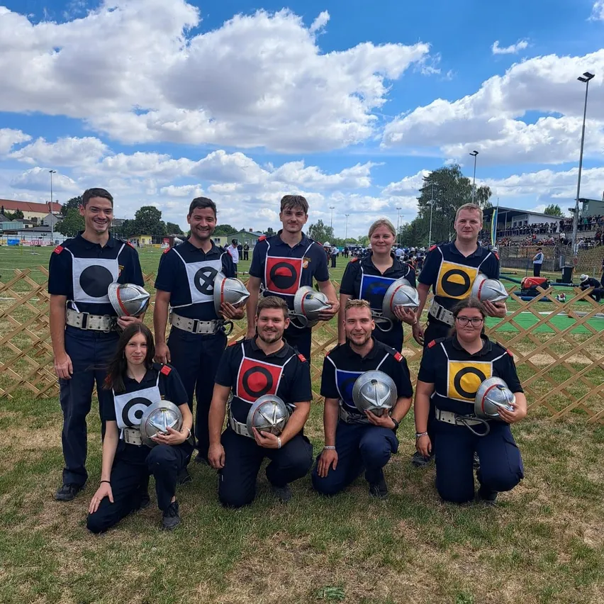 Eine Gruppe von Menschen in Uniformen und Helmen posiert für ein Foto auf einem Feld mit einem Zaun im Hintergrund.