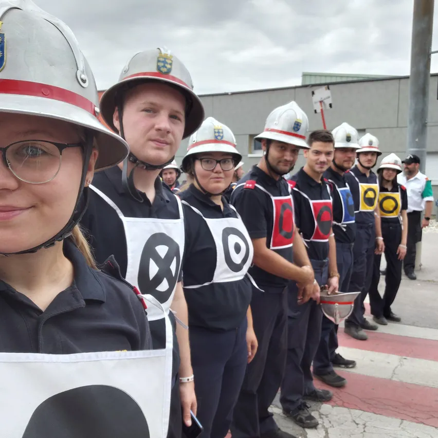 Eine Gruppe von Feuerwehrleuten in Uniformen und Helmen steht in einer Reihe, einige tragen Helme. Die Frau vorne trägt eine Brille und ein weißes Uniform.