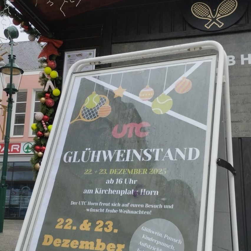 Ein Schild vor einem Geschäft bewirbt einen 'Glühweinstand' am 22. und 23. Dezember 2025, um 16 Uhr am Kirchenplatz Horn. Das Schild zeigt Tennisbälle und Dekorationen.
