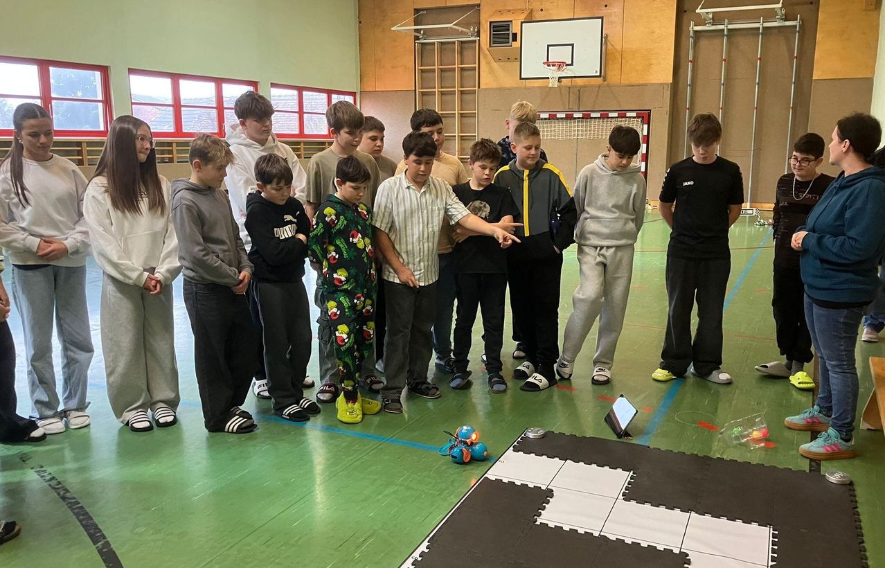 Eine Gruppe Jungen in einer Turnhalle mit einem Basketballkorb und einem Roboter auf dem Boden.