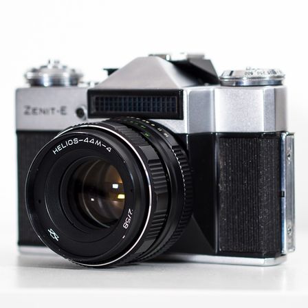 Eine schwarze und silberne Kamera mit einem schwarzen Objektiv steht auf einer weißen Oberfläche.