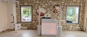 Ein Raum mit einer Steinmauer, einer Glastür und einem Lautsprecher-Setup mit Laptop. Es gibt zwei runde Wanddekorationen mit Blumen und einem rosa Licht.