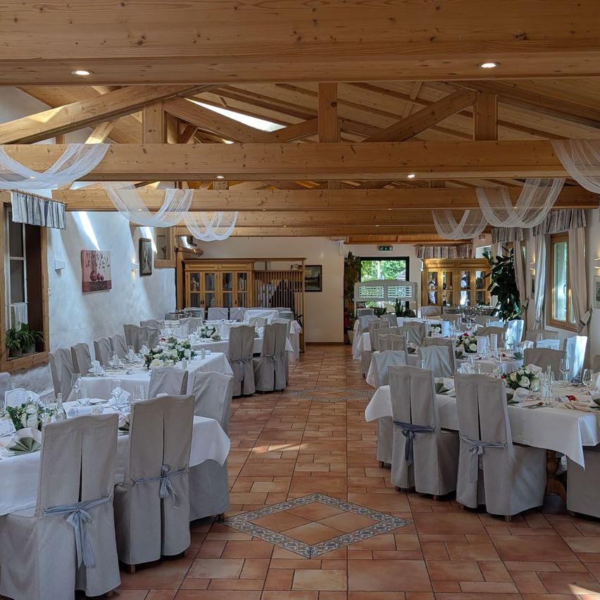A well-decorated indoor dining area with wooden beams and terracotta tiles, featuring multiple tables set for a formal event.
