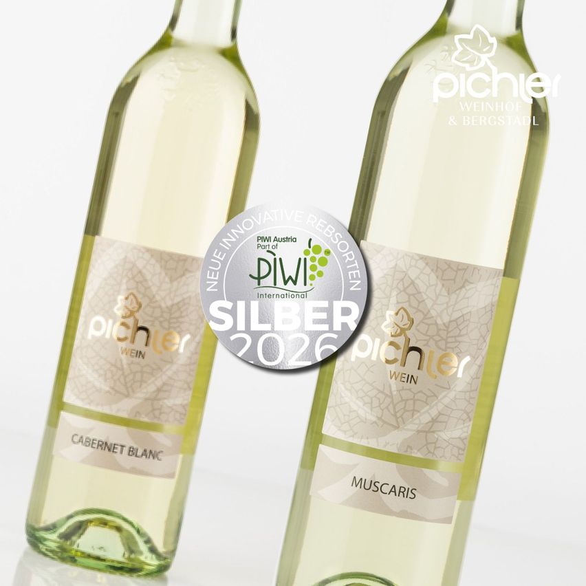 Zwei Flaschen Wein, beschriftet mit Cabernet Blanc und Muscaris, präsentiert mit einem silbernen Auszeichnungssiegel. Die Flaschen haben weiße Etiketten auf einem grünen Hintergrund.