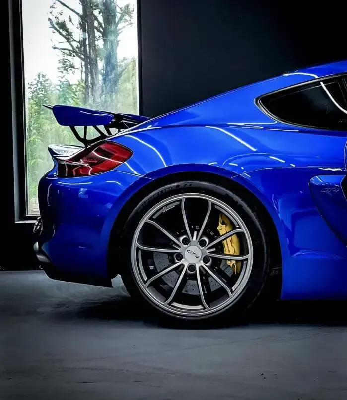 Ein blauer Sportwagen mit Spoiler in einer Garage geparkt, mit Blick auf Bäume draußen.