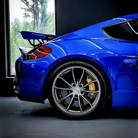 Ein blauer Sportwagen mit Spoiler in einer Garage geparkt, mit Blick auf Bäume draußen.