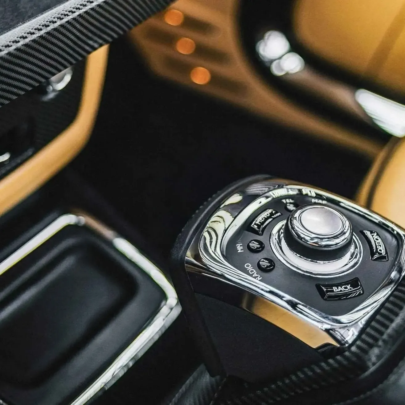 Nahaufnahme eines Auto-Gangschalters, silber und schwarz, mit einer Taste, die 'BACK' beschriftet ist, vor einem schwarzen und beigen Innenraum.