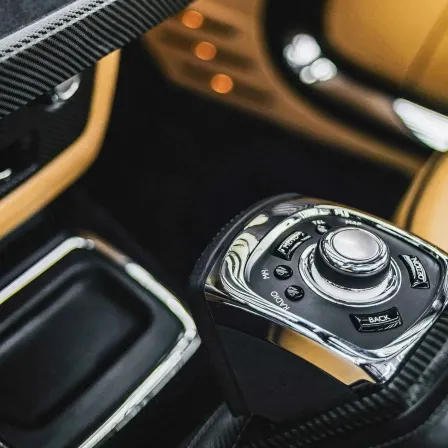 Nahaufnahme eines Auto-Gangschalters, silber und schwarz, mit einer Taste, die 'BACK' beschriftet ist, vor einem schwarzen und beigen Innenraum.