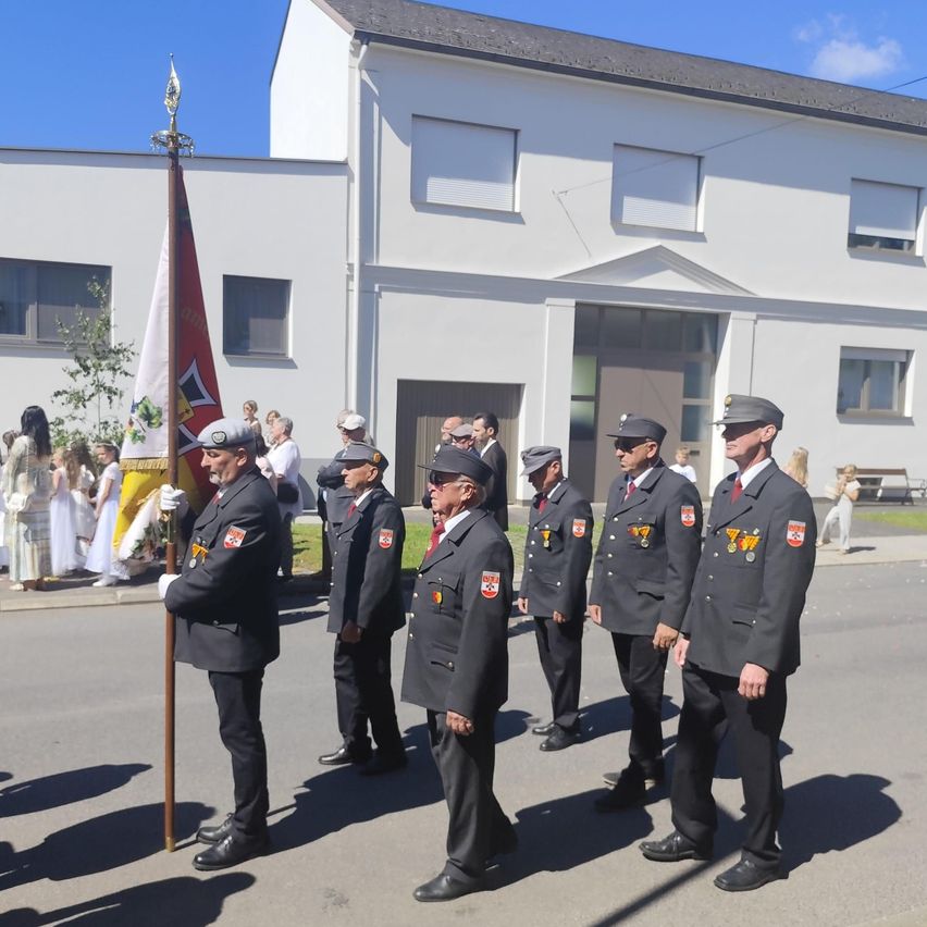 Five uniformed men stand in front of a building with a flag. Behind them, a few people stand and watch.
