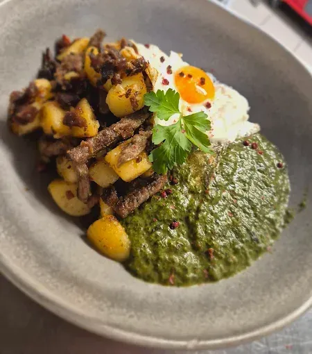 Ein Teller mit Rösti, einem Spiegelei und grüner Sauce obenauf.