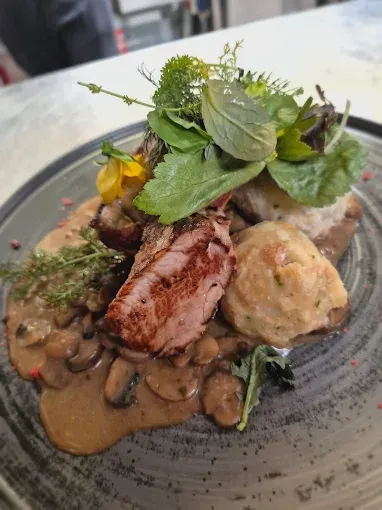 Ein Teller mit Fleisch, Knödeln und Gemüse. Das Fleisch ist mit Sauce bedeckt.