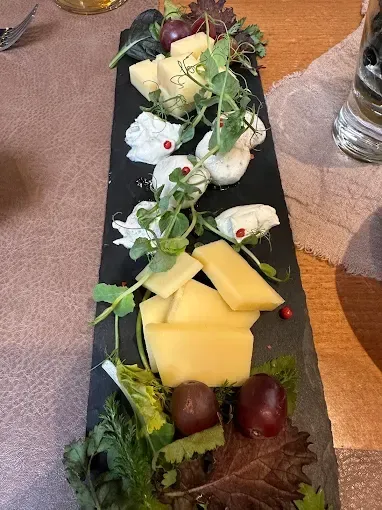 Ein Käsetablett mit verschiedenen Käsesorten, Trauben und Blattgemüse ist auf einem Holztisch ausgestellt.