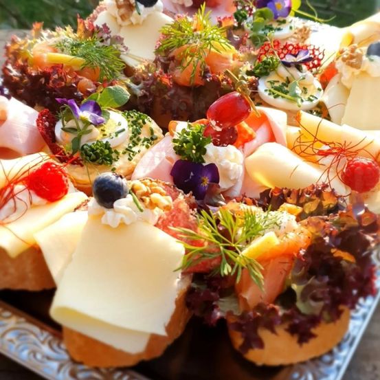 Eine Nahaufnahme eines Buffettisches mit verschiedenen Brot-, Käse- und Fleischsandwiches, garniert mit Blumen und Früchten.