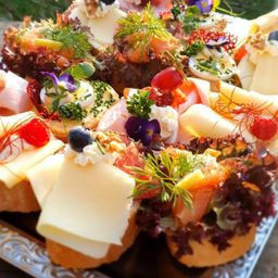 Eine Nahaufnahme eines Buffettisches mit verschiedenen Brot-, Käse- und Fleischsandwiches, garniert mit Blumen und Früchten.