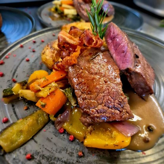 Ein Teller mit Steak und Gemüse in Sauce, begleitet von Kartoffeln und einem Rosmarinzweig.