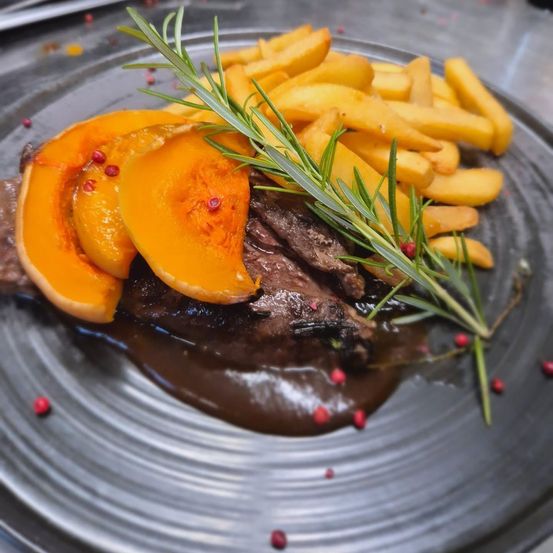 Gegriltes Steak mit Kürbisscheiben, roten Pfefferflocken und Rosmarin auf einem Teller mit Pommes frites.