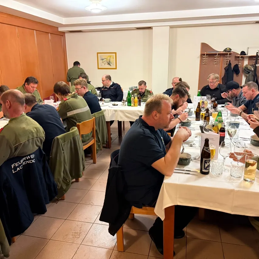 Eine Gruppe von Männern, einige in Uniformen, sitzt an einem langen Tisch mit Getränken und Essen, scheinbar in einer Besprechung oder Versammlung.