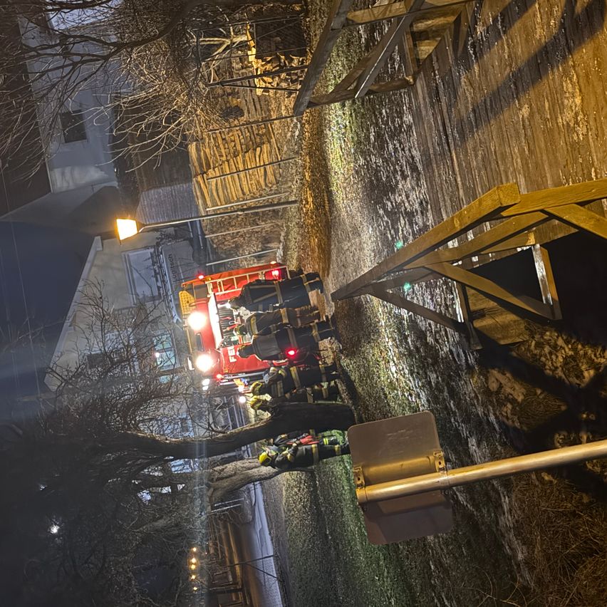 Firefighters in protective gear are standing near a red fire truck with flashing lights on a street at night.