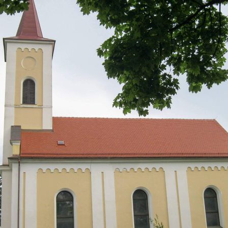 Eine gelbe und weiße Kirche mit einem roten Dach und einem Turm mit einem runden Fenster.