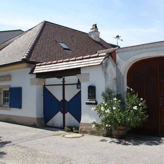 Ein kleines traditionelles Haus mit einem braunen Dach und blauen Fensterläden. Eine blaue und weiße Tür befindet sich auf der linken Seite.