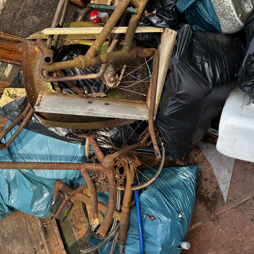 Ein Blick von oben auf einen Müllhaufen mit einem verrosteten Fahrradrahmen, Plastiktüten und einem Holzbrett.
