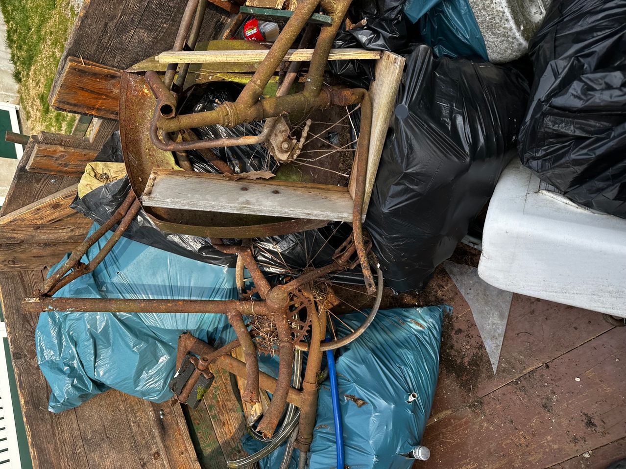 Ein Blick von oben auf einen Müllhaufen mit einem verrosteten Fahrradrahmen, Plastiktüten und einem Holzbrett.