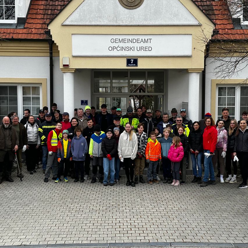 Eine Gruppe von Erwachsenen und Kindern steht vor dem Gemeindeamt Opcinski Ured-Gebäude, alle in Winterkleidung und Handschuhen.
