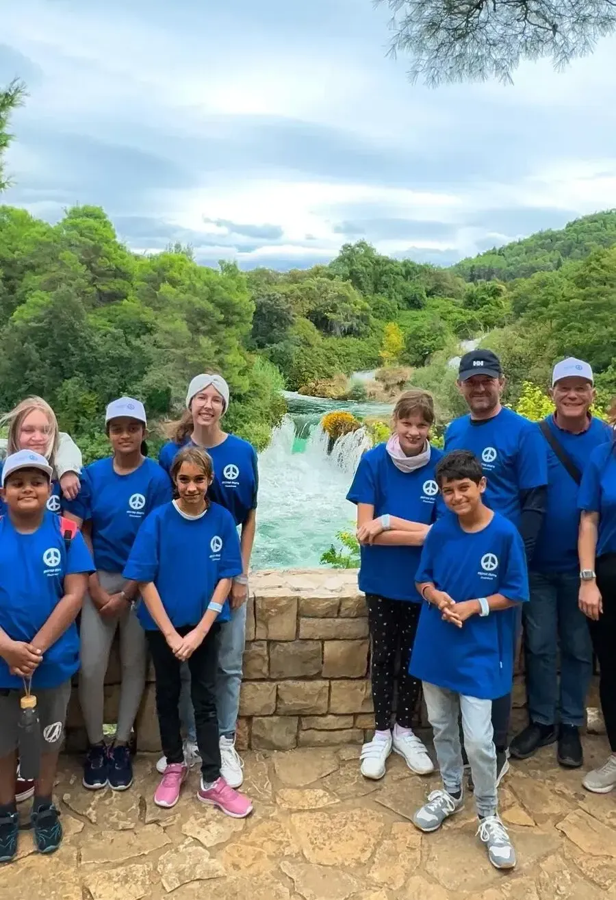 Eine Gruppe von Menschen in blauen T-Shirts mit einem Friedenssymbol posiert vor einem Wasserfall und einer Steinmauer.