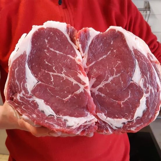 Eine Person in einem roten Shirt hält zwei große Stücke rohes Rindfleisch in den Händen.
