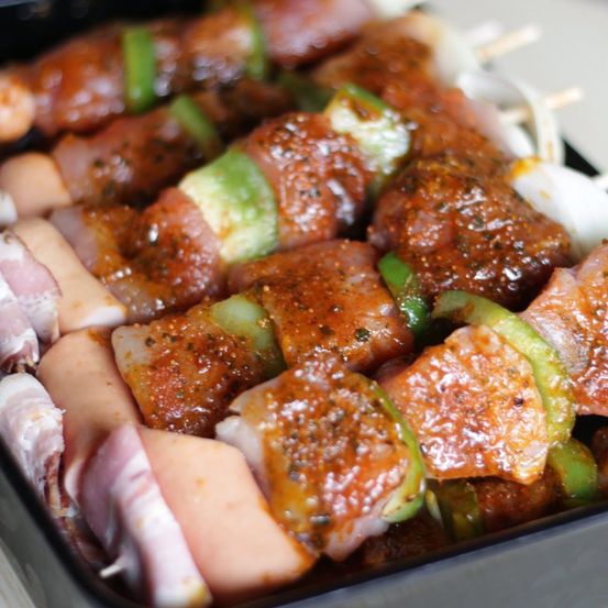 Nahaufnahme von Spießfleisch, einschließlich Würstchen und Schinken, mit roter Glasur und grünen Paprika garniert.